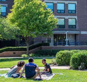Three students relax on a green lawn on campus.
