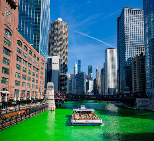 A river dyed vibrant green and flanked by tall city buildings