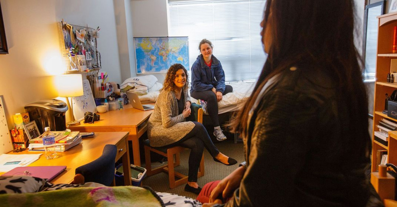 Three young women relax in dorm room. 
