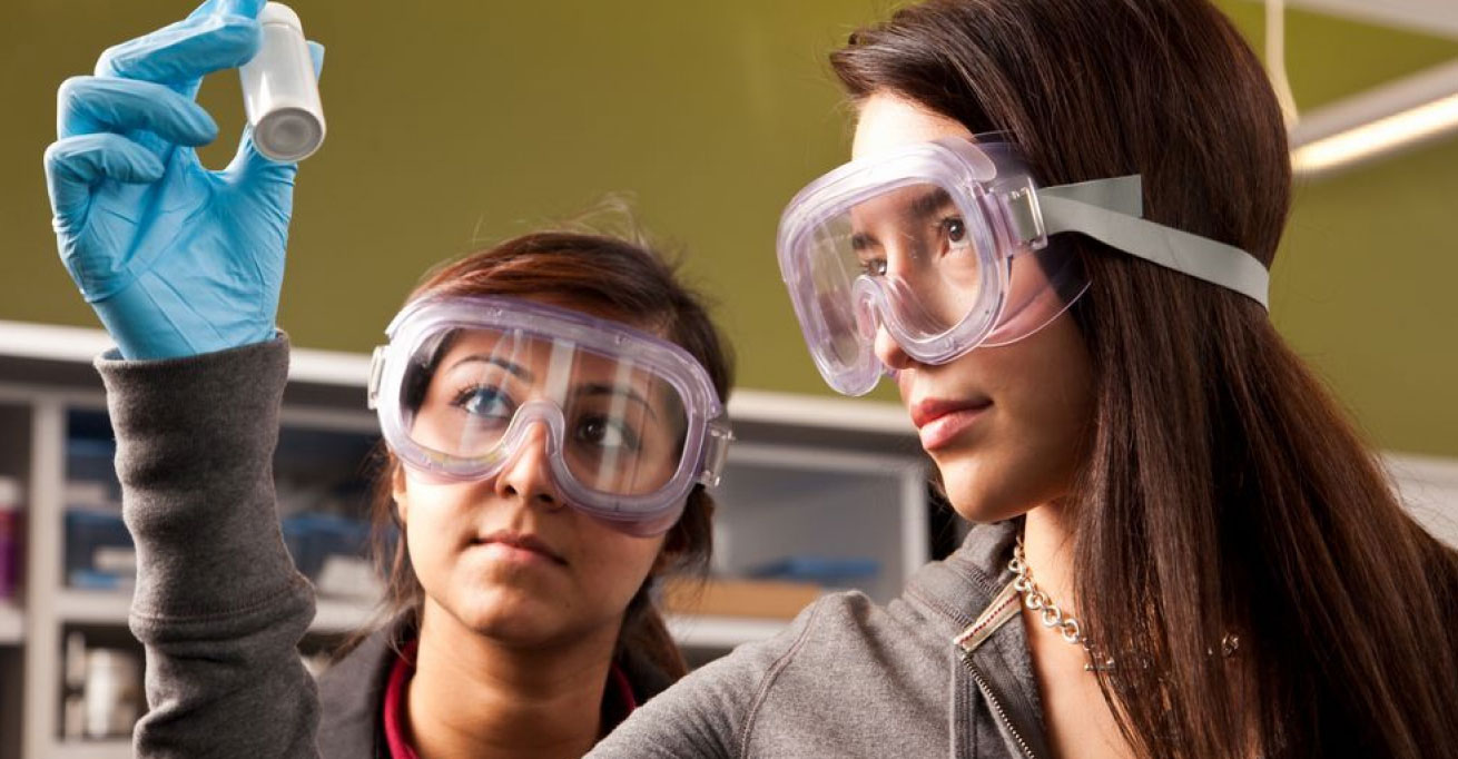 Two young women examine a vial in a lab